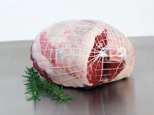 Boneless leg of lamb tied in butcher’s netting, resting on a metal surface with a sprig of herbs.