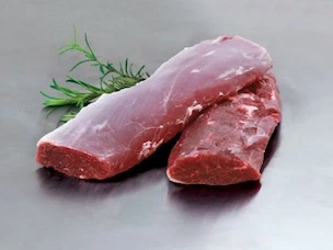 Two pieces of raw lamb eye of loin on a metal surface with a sprig of fresh herbs.